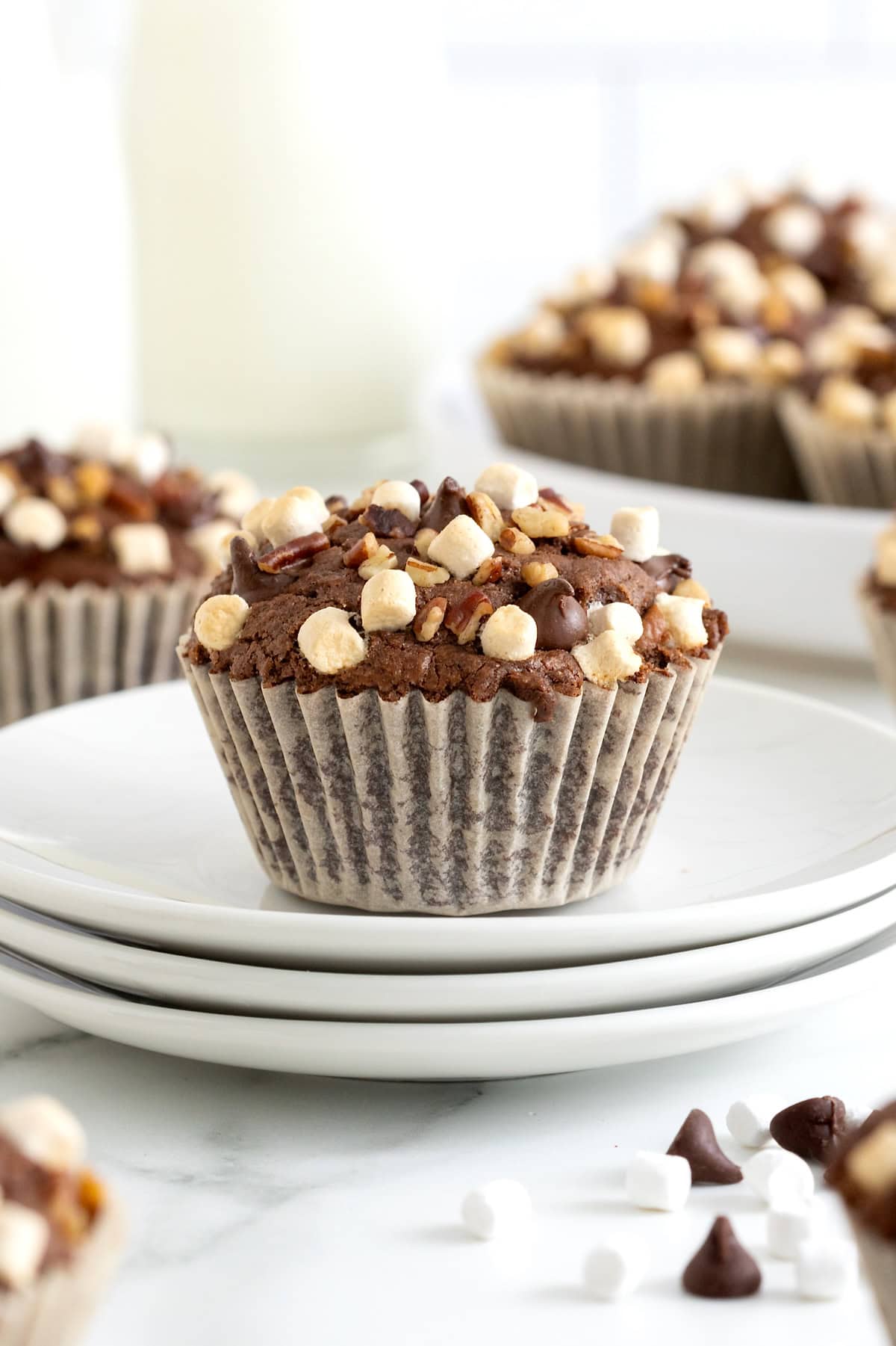 A rocky road brownie cupcake on a stack of three white plates.
