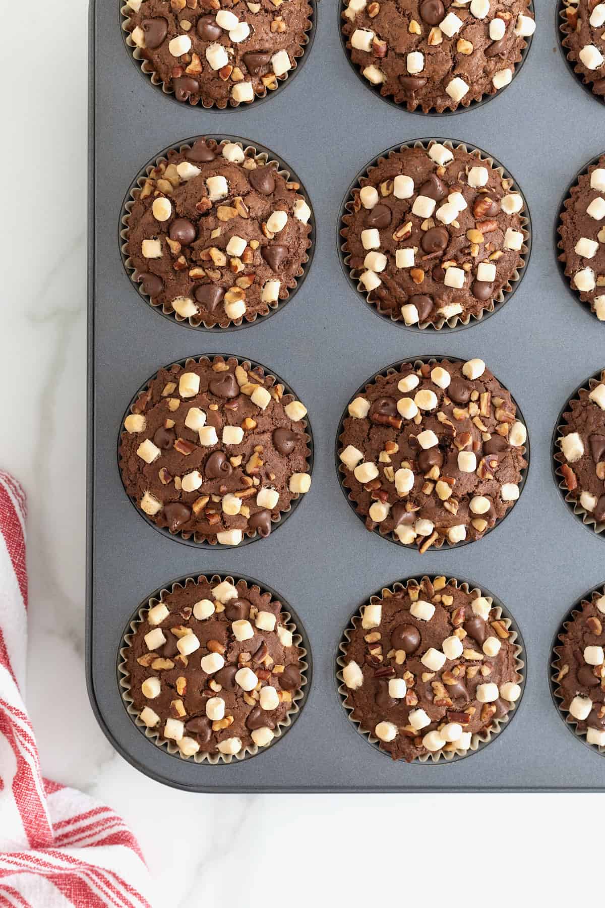 12 rocky road brownie cupcakes in a dark aluminum muffin pan.