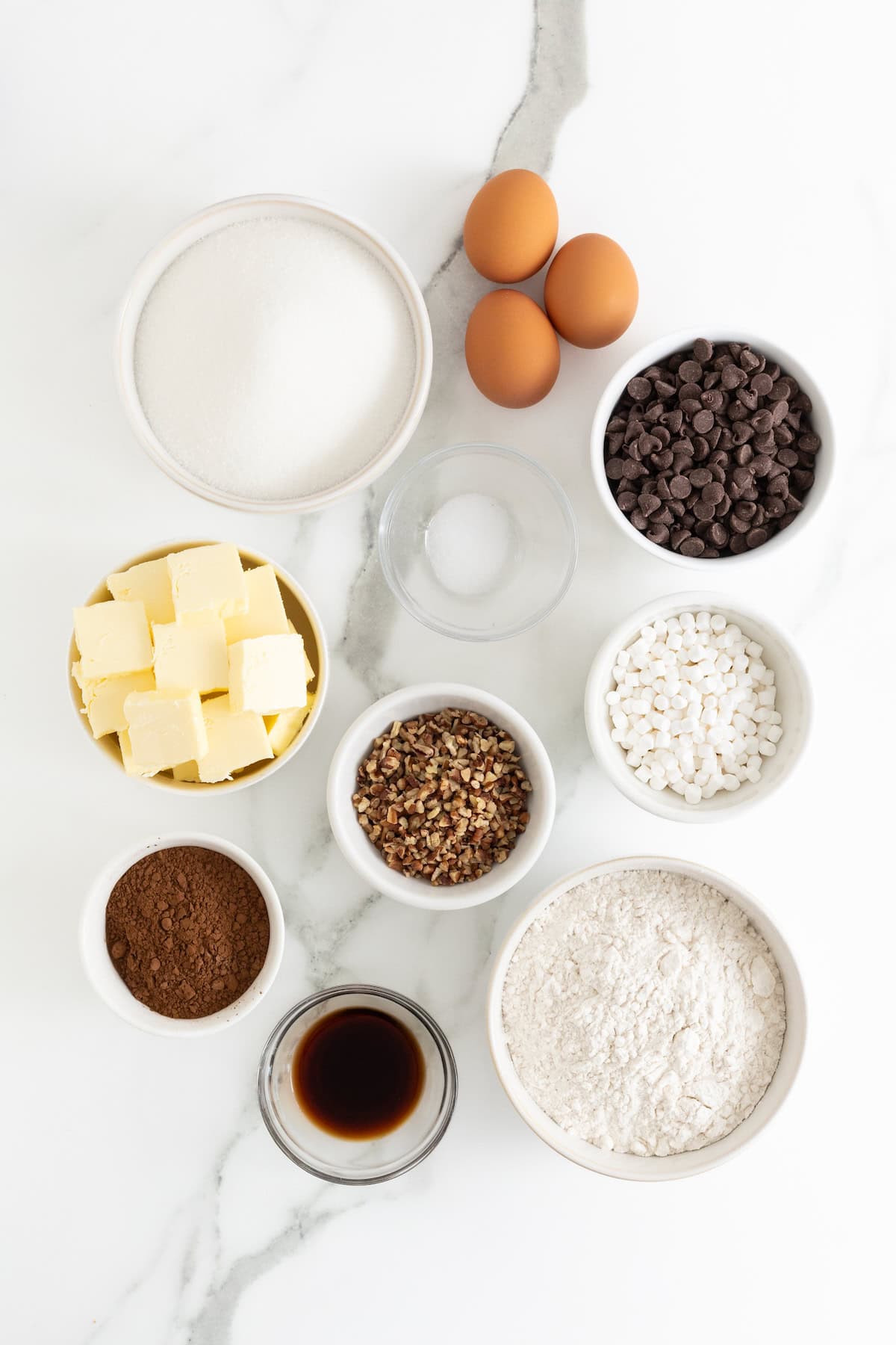 Ingredients to make rocky road brownie cupcakes in white dishes on a white marble counter.