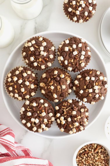 A white platter of Rocky Road Brownie Cupcakes garnished with freeze-dried mini marshmallows and chocolate chips.