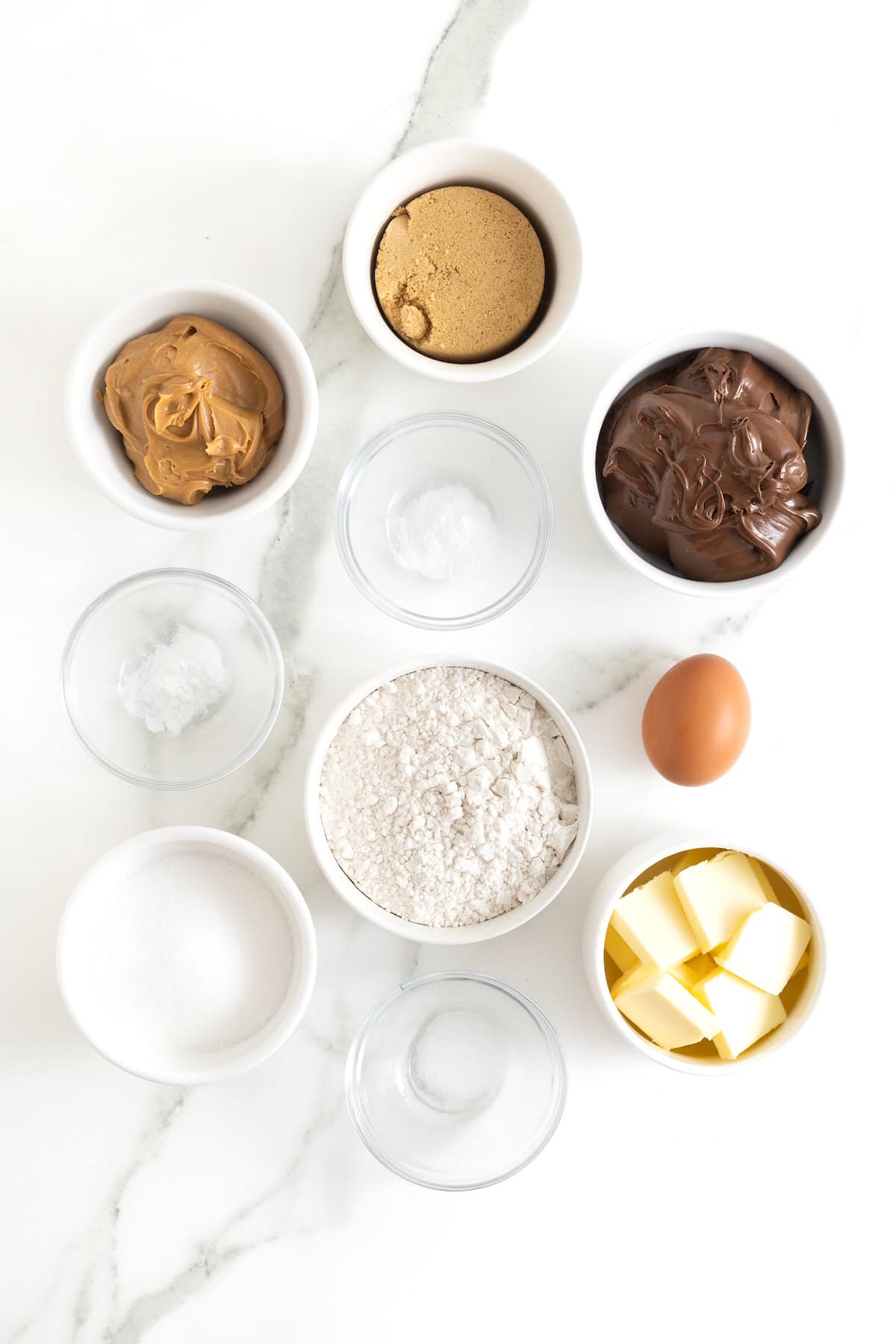 Ingredients to make peanut butter sandwich cookies in small glass dishes on a white marble counter.