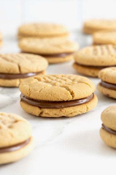 10 peanut butter cookie sandwiches with a chocolate hazelnut filling on a white marble surface.