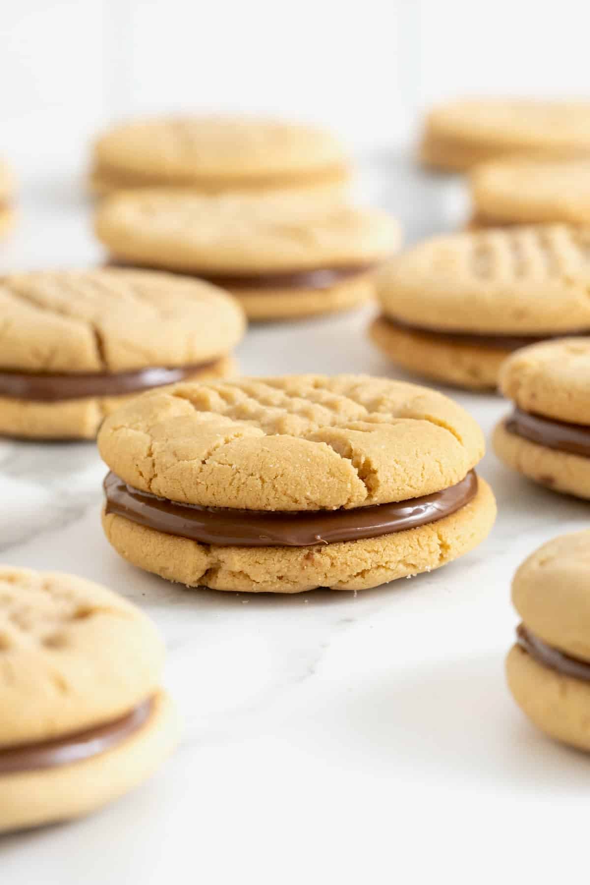 10 peanut butter cookie sandwiches with a chocolate hazelnut filling on a white marble surface.