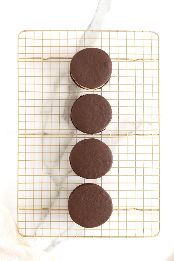Chocolate cookies with peanut butter cream on a gold toned cooling rack.