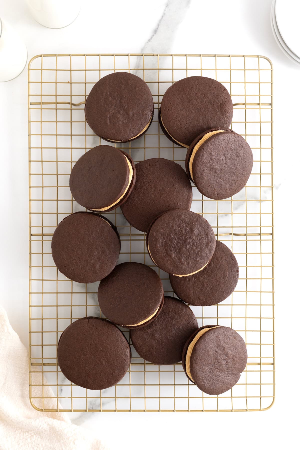 A pile of chocolate sandwich cookies filled with peanut butter cream on a gold toned wire cooling rack.