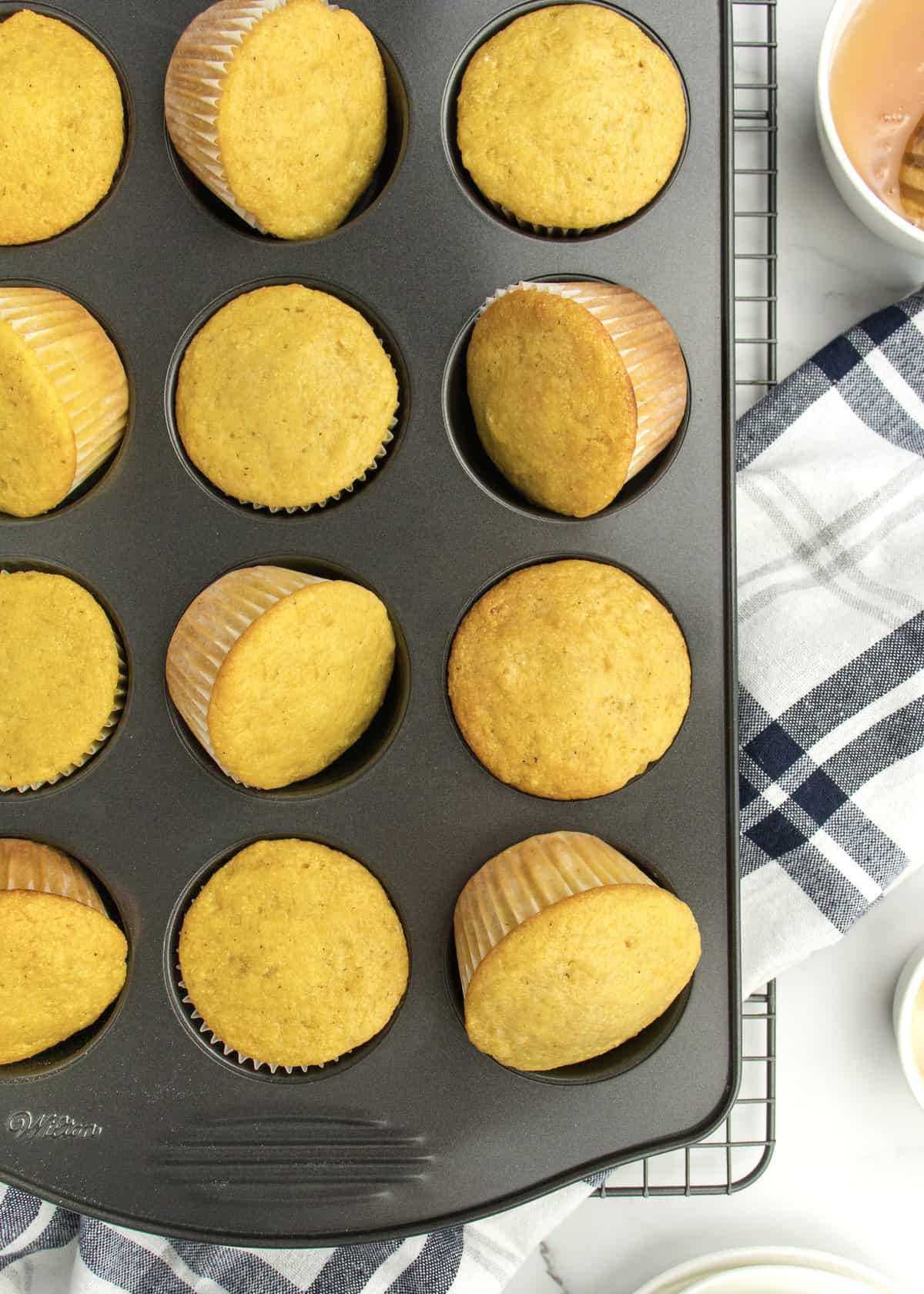 Honey corn muffins in a 12-cup dark muffin tin. Some of the muffins are tipped on their sides.