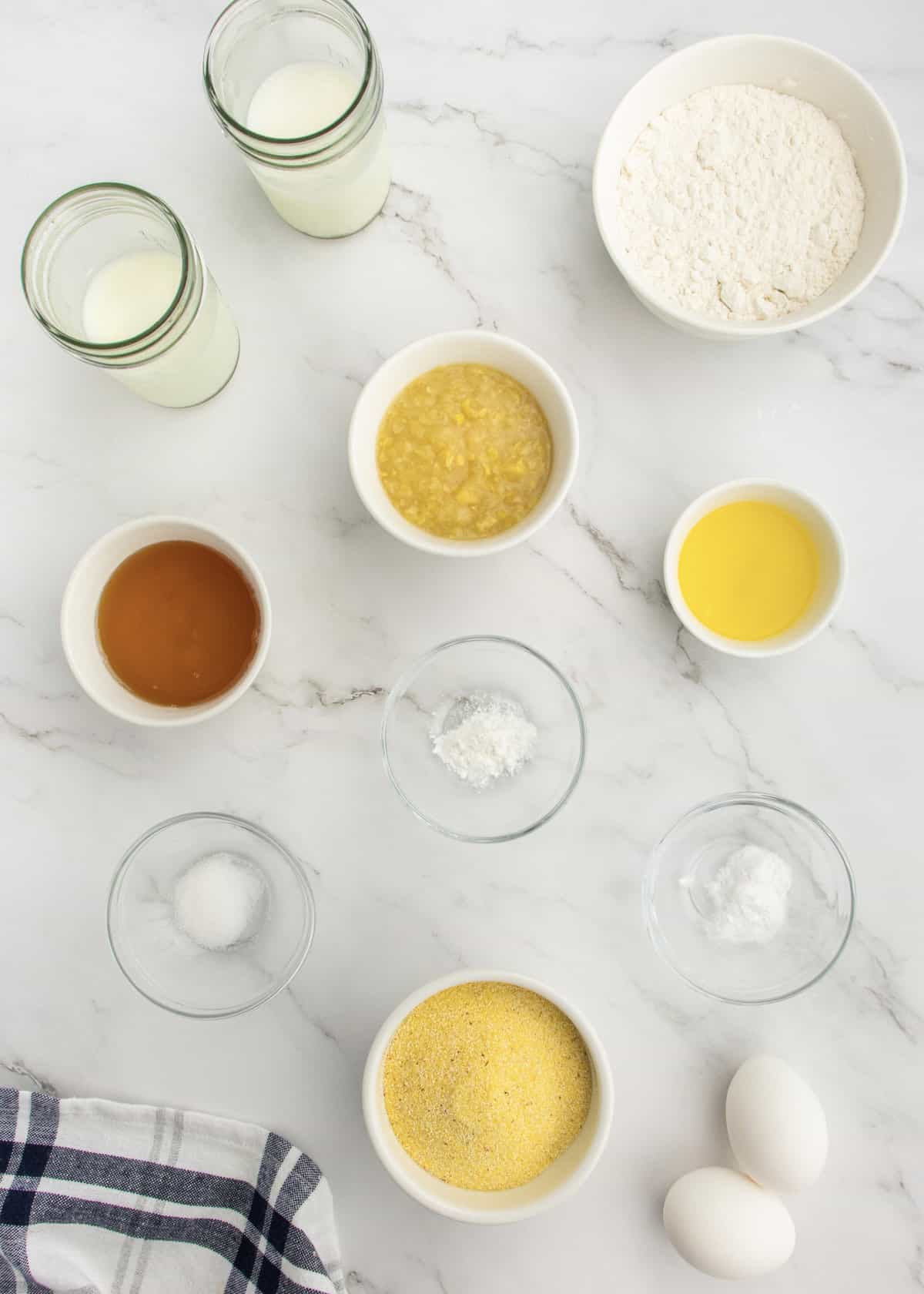 Ingredients for honey corn muffins in small glass dishes on a white marble counter.