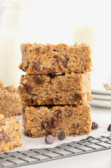 Three square granola bars with chocolate chips stacked on a serving plate.
