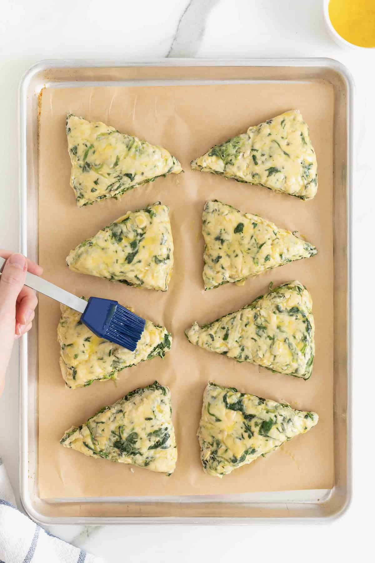Scones being brushed with an egg wash using a blue silicon food brush.