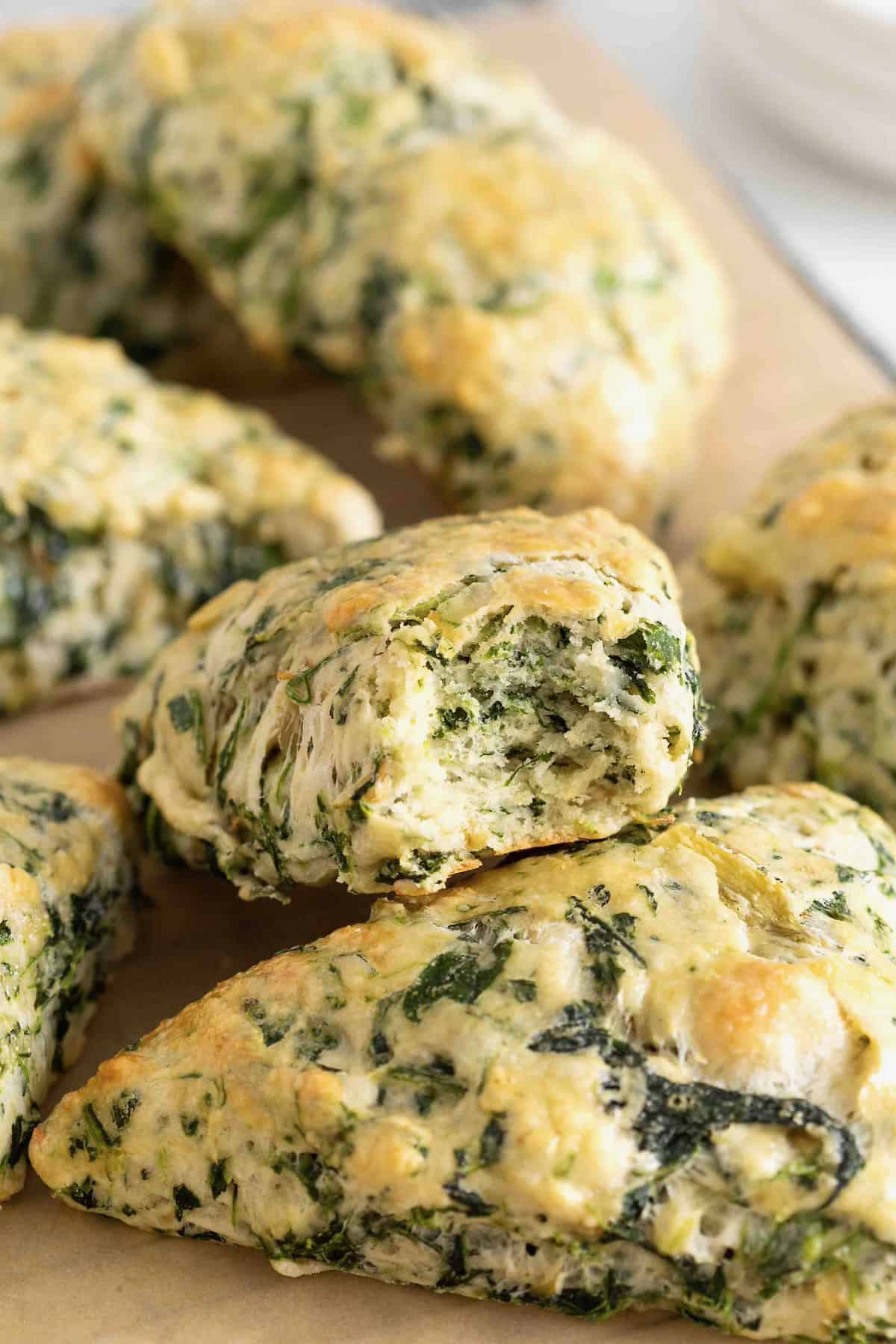 A pile of spinach artichoke scones. The top scone has a bite out of it.