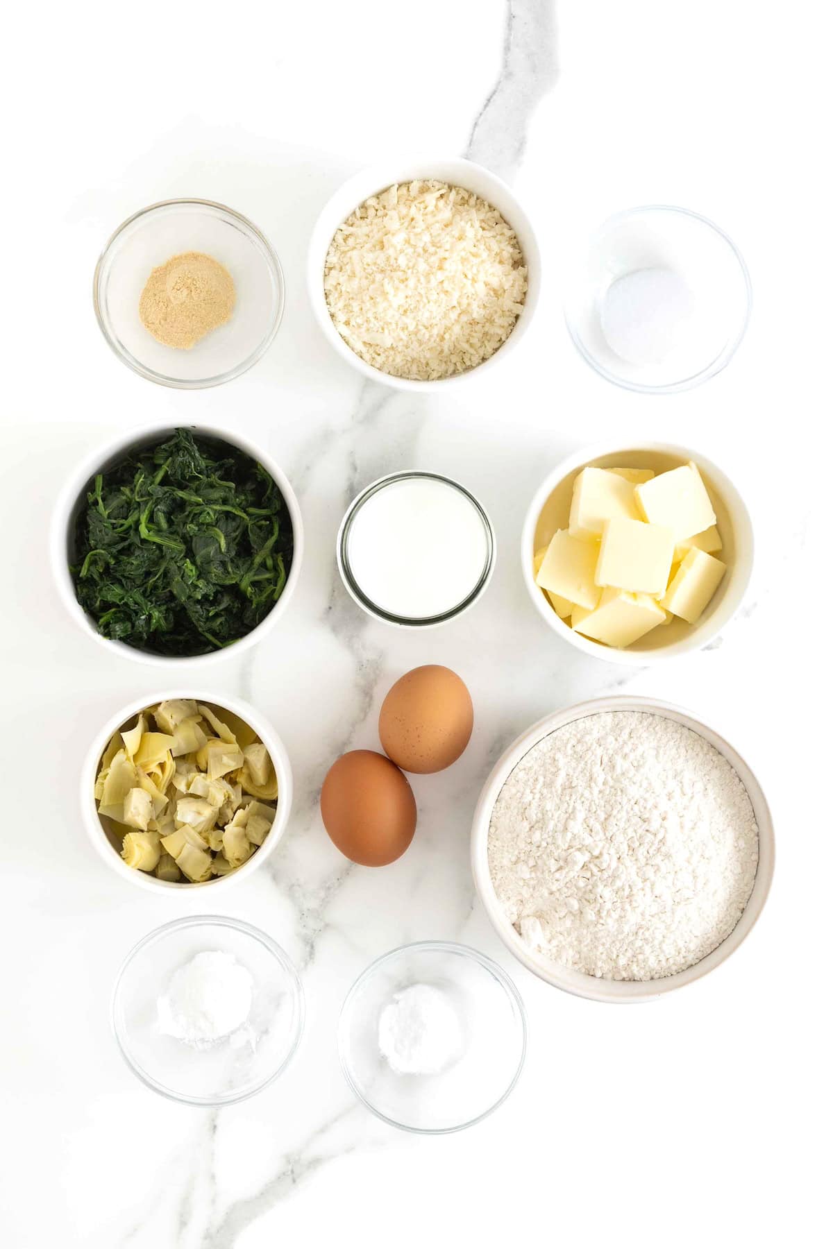 Ingredients to make spinach artichoke scones in small glass dishes on a white marble counter.