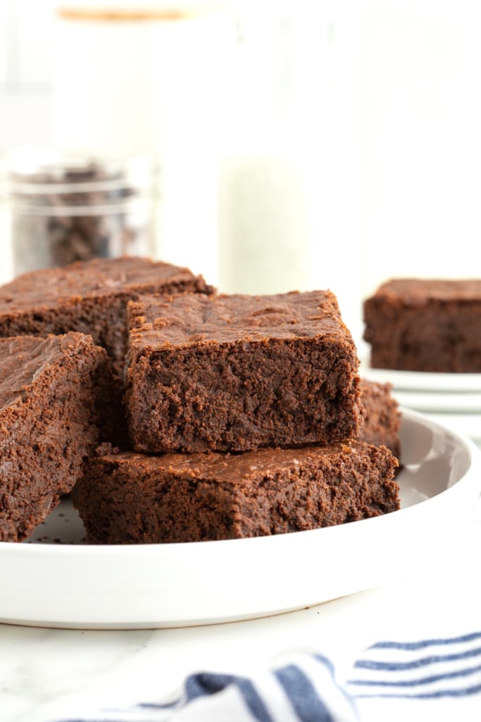 A large white round rimmed serving plate with four brownies in a pile.