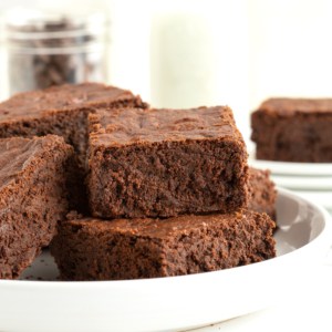 A large white round rimmed serving plate with four brownies in a pile.