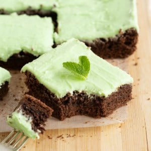 Brownies with light green mint frosting on a parchment lined cutting board.