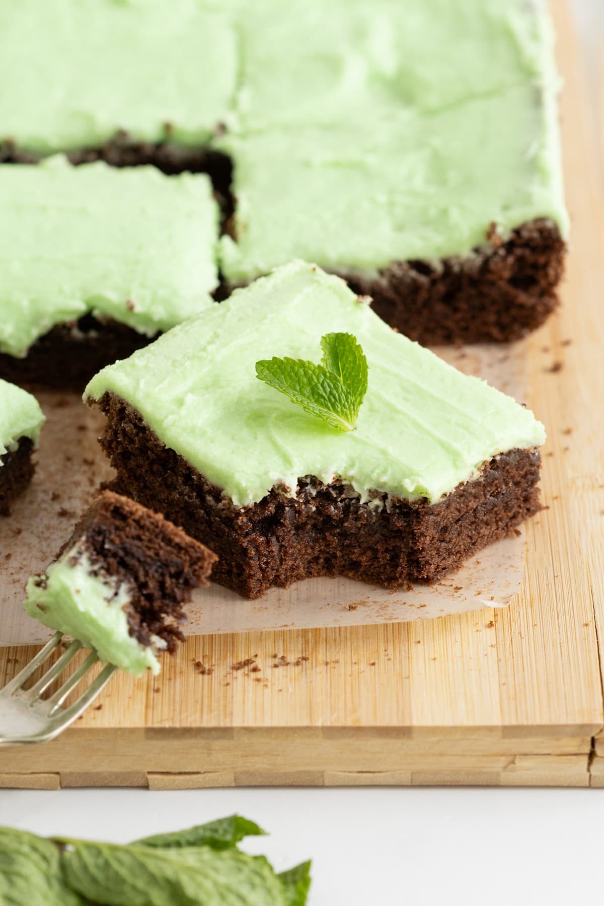 Brownies with light green mint frosting on a parchment lined cutting board.