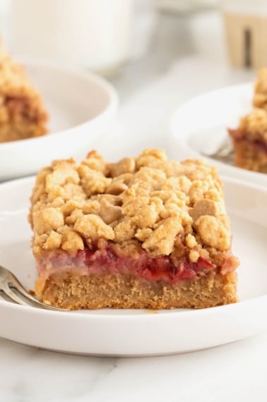 A strawberry peanut butter bar on a white rimmed plate with a fork.
