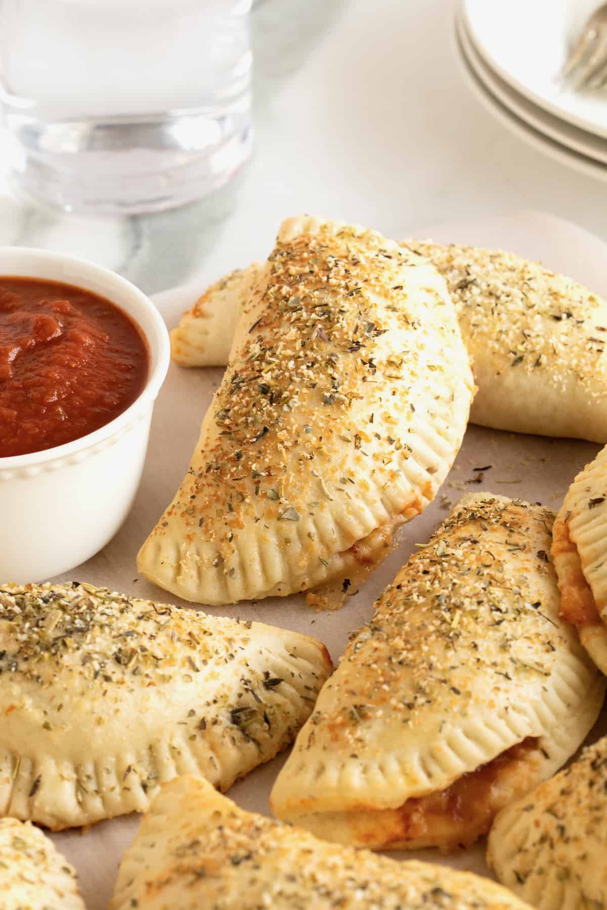 Five mini calzones on a white plate next to a small dish of marinara sauce.