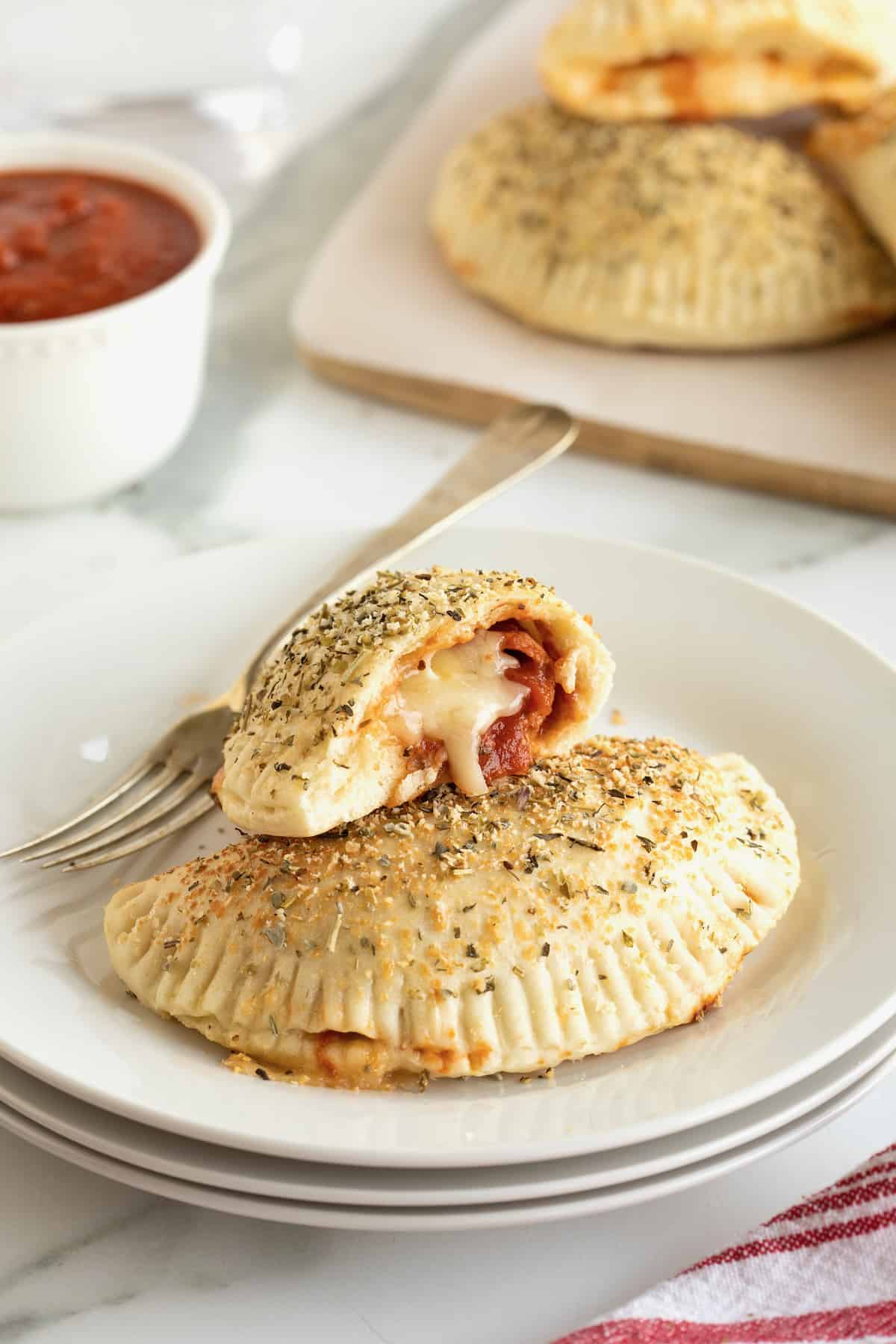 A mini pepperoni calzone and a half eaten calzone on a white plate with a fork. 