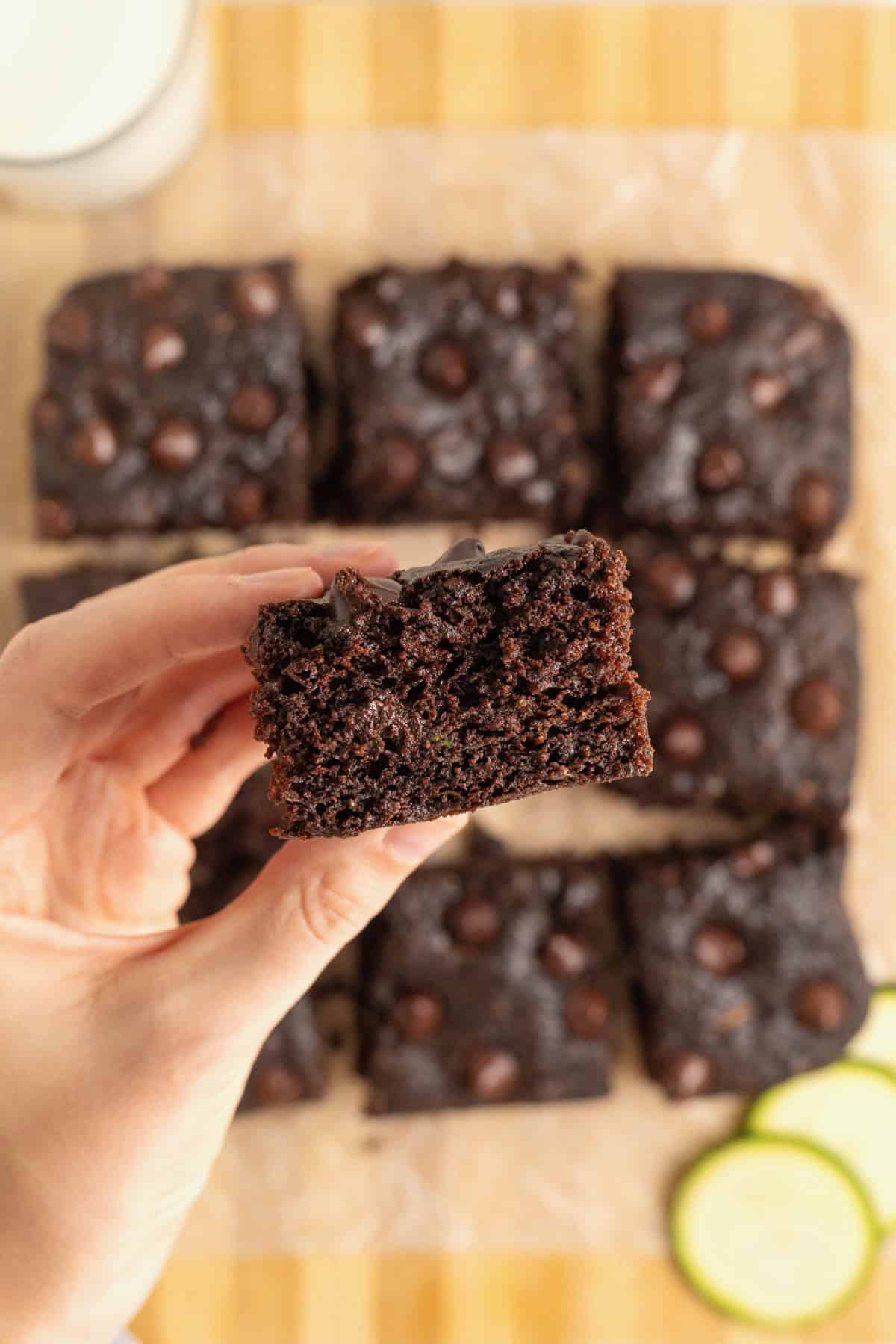 A hand picking up a brownie off a light wood cutting board of brownies.