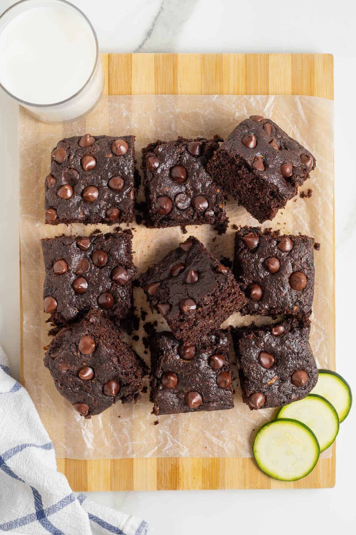 Dark chocolate zucchini brownies on a parchment lined wooden cutting board.