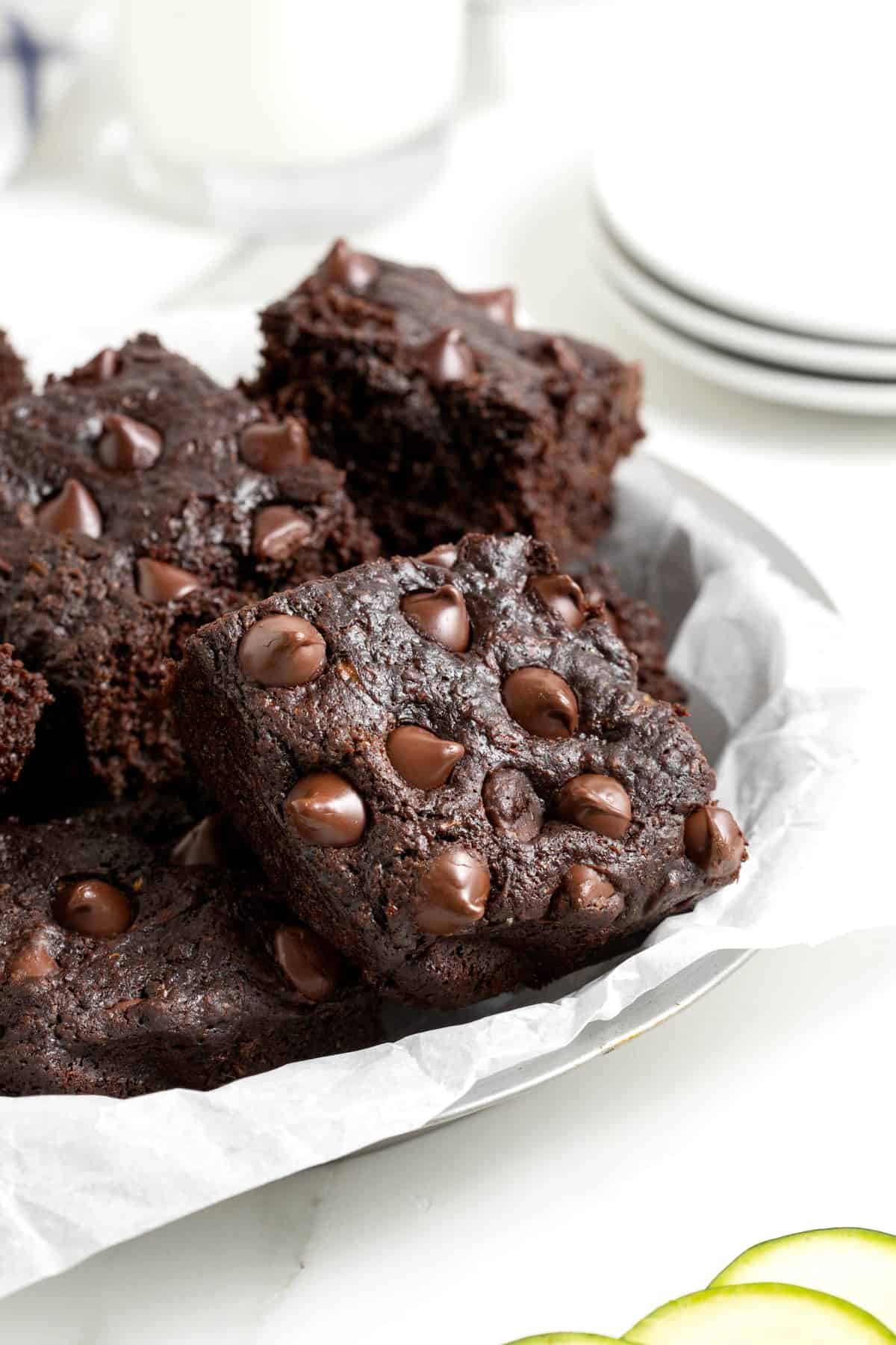 A white plate piled with dark chocolate zucchini brownies on a white marble counter.