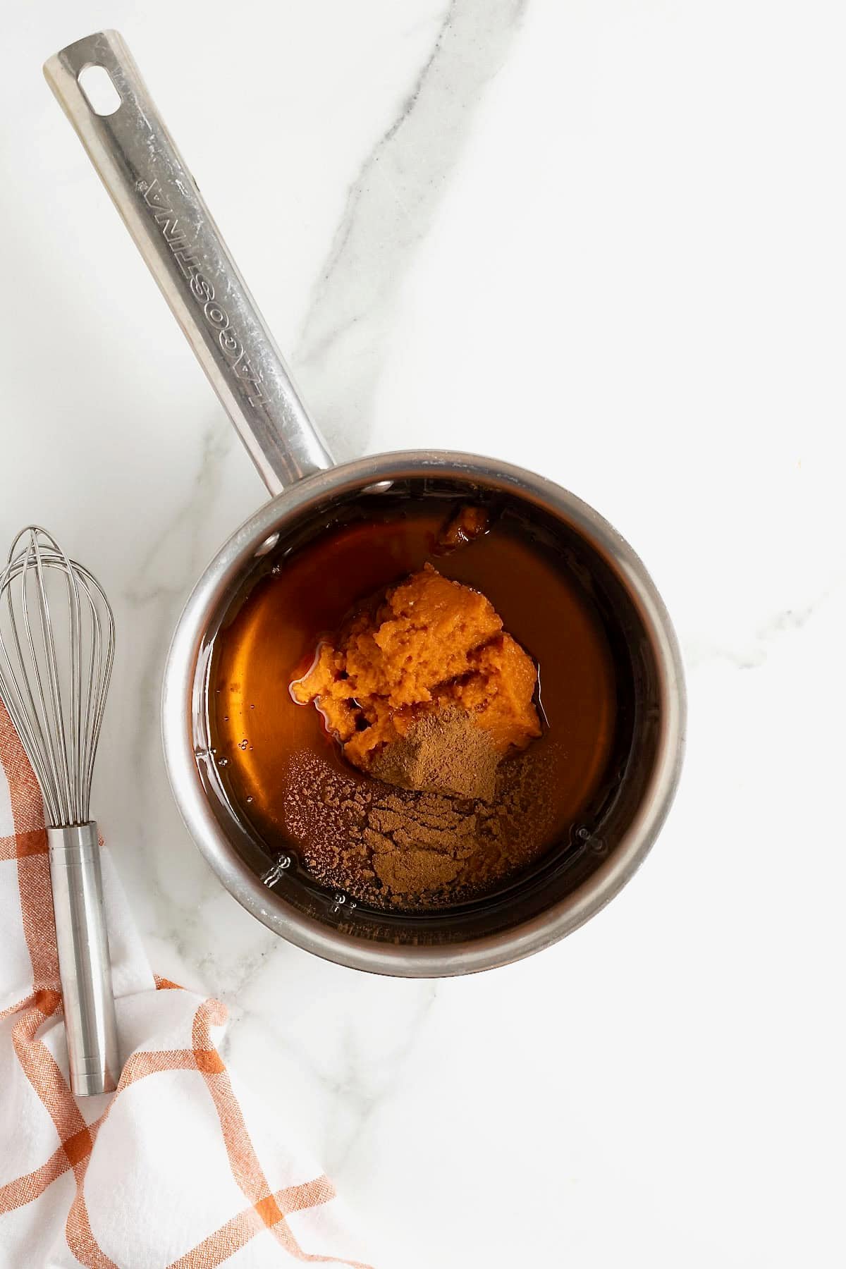 Pumpkin puree, maple syrup and pumpkin spice in a metal saucepan.
