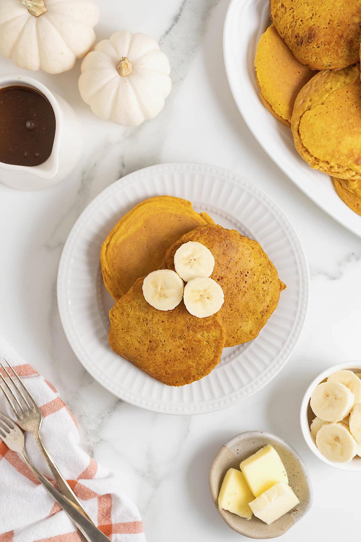 Three pumpkin banana pancakes on a white plate. There are three banana slices on the pancakes.