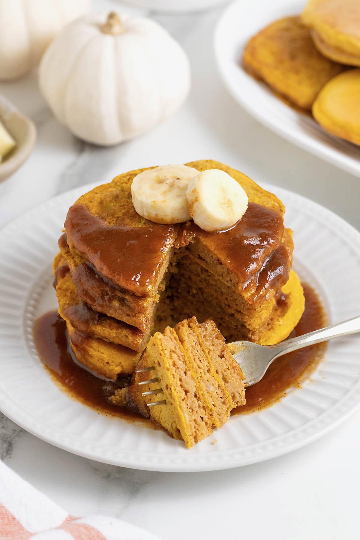 A stack of four pumpkin banana pancakes with a bite taken out.