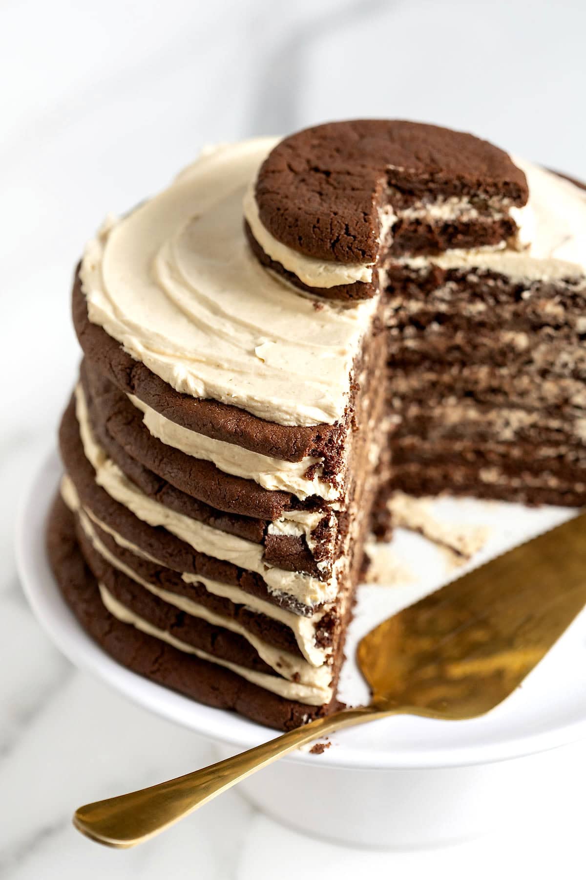 A chocolate layer cake with peanut butter icing on a white cake stand. There are slices cut out of the cake. A metal pastry server is on the cake stand.