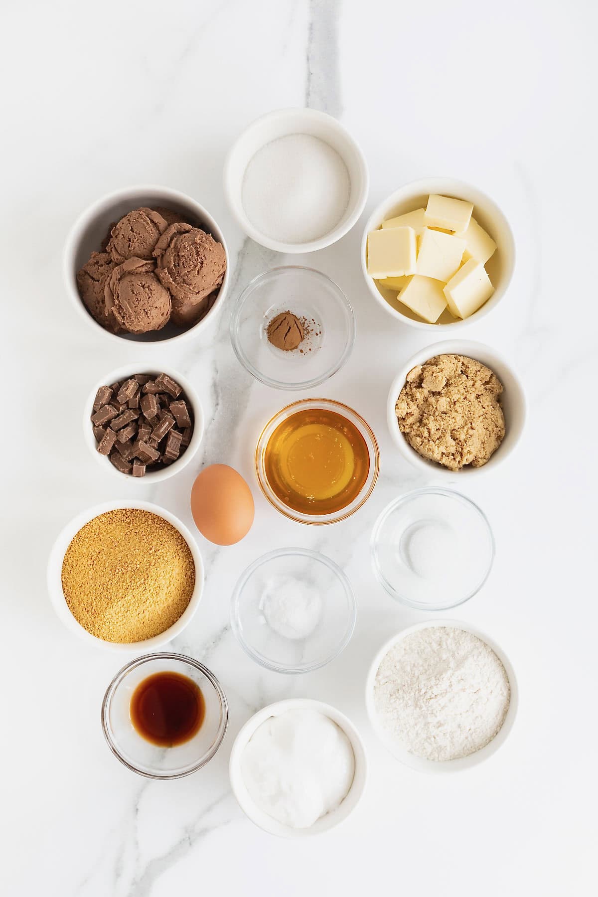 Ingredients to make s'mores ice cream sandwiches in small glass dishes on a white marble counter.