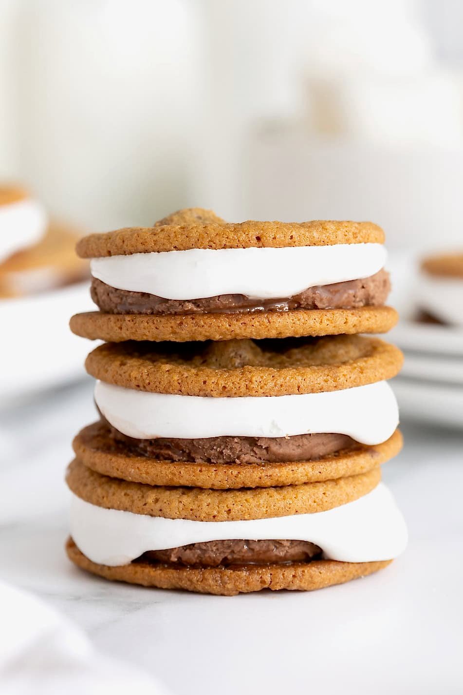 A stack of three s'mores ice cream sandwiches on a white marble surface.