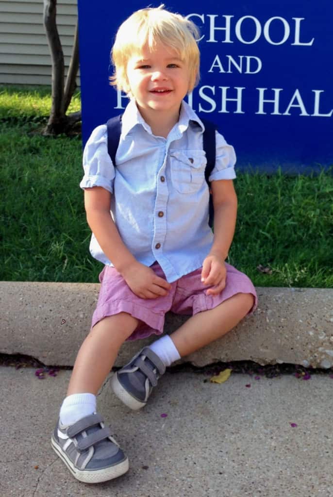 A small child with white blonde hair sitting in front of a blue sign with white lettering.