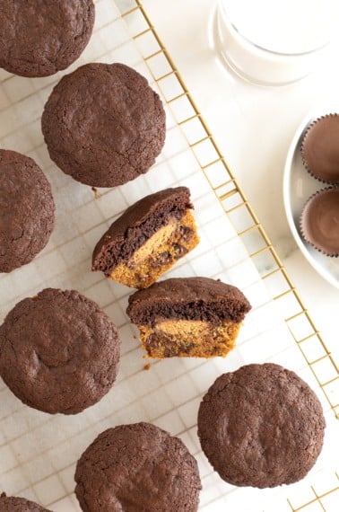 A muffin-shaped treat with a cookie bottom, a brownie top and a peanut butter cup in the middle cut in half laying on a parchment lined cooling rack.
