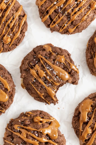 Seven chocolate cookies drizzle with caramel on a white surface.