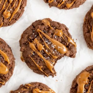 Seven chocolate cookies drizzle with caramel on a white surface.