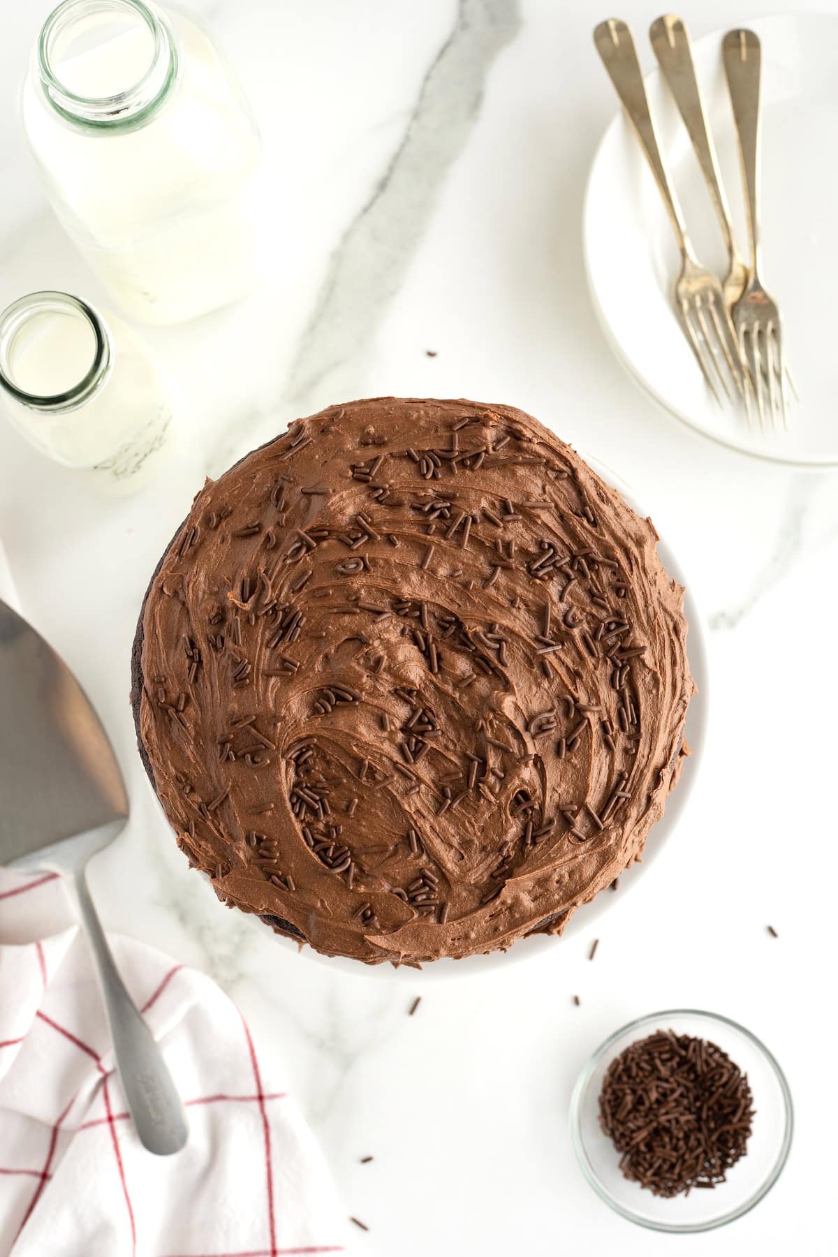 View of the a chocolate cake with chocolate icing and chocolate sprinkles from the top on a white marble counter.
