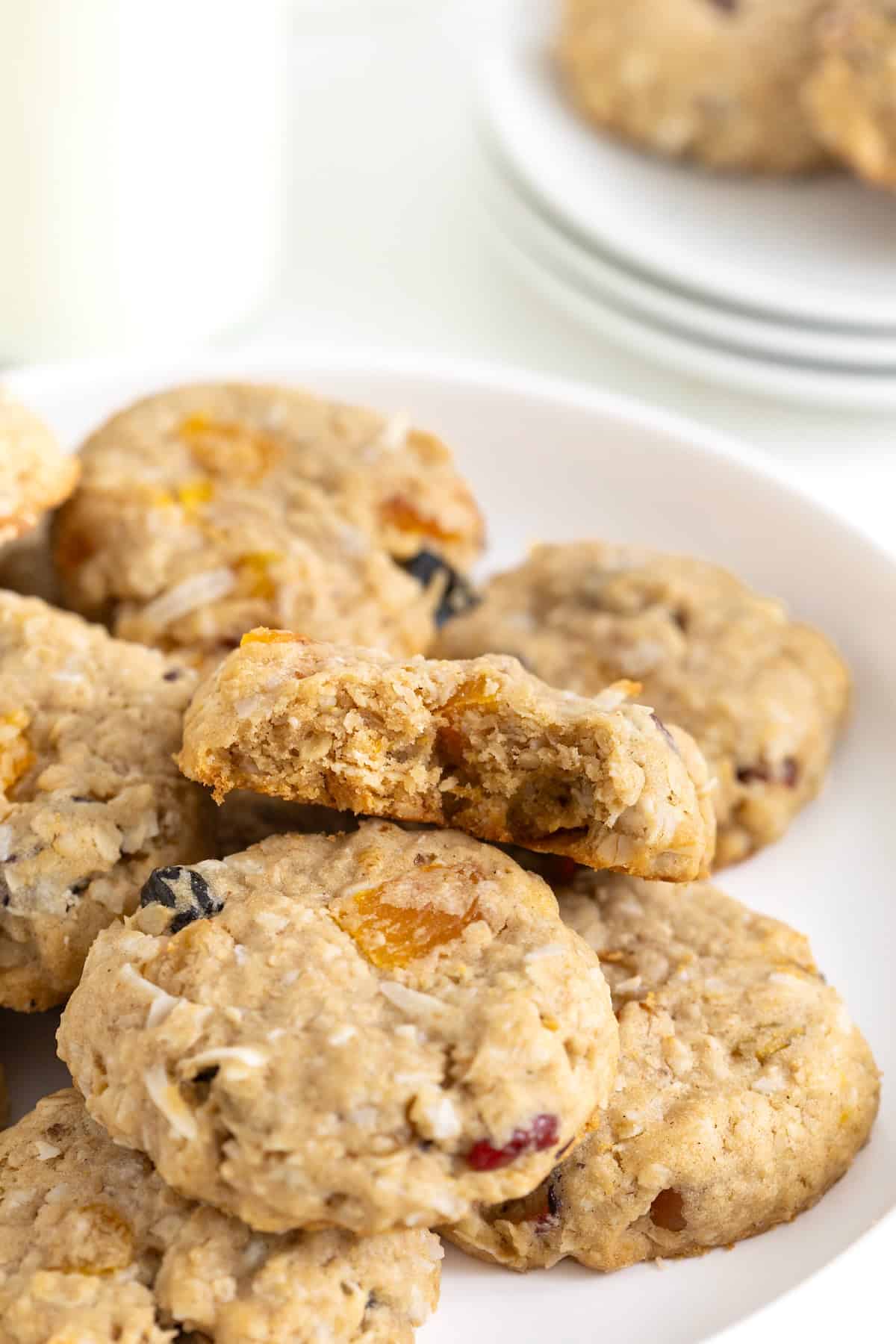 A pile of coconut oatmeal cookies on a white plate. The top cookie has a bite out of it.