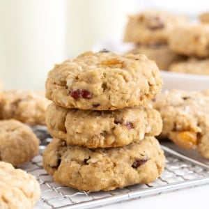 Three coconut oatmeal cookies stacked on a wire cooling rack.