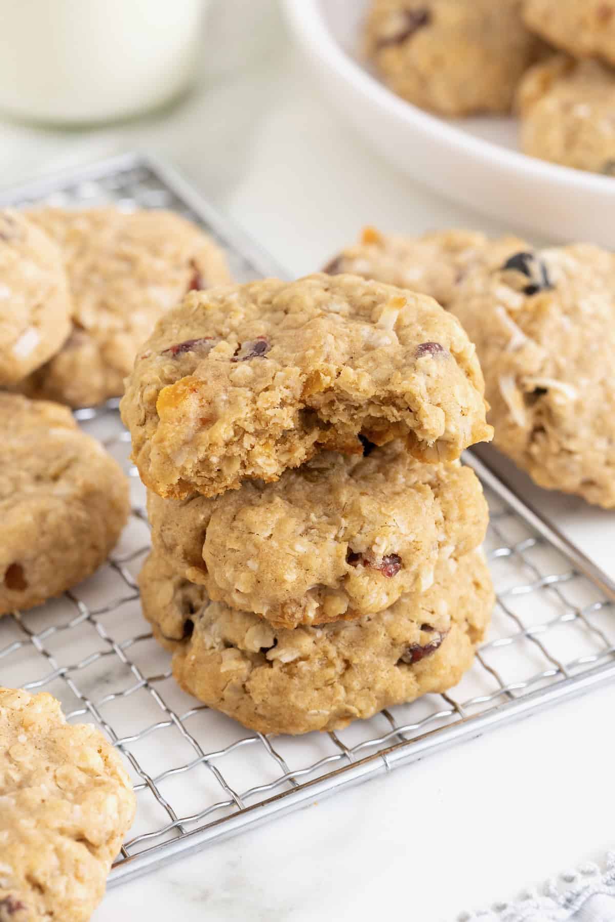 Three coconut oatmeal cookies stacked on a wire cooling rack. The top cookie has a bite out of it.