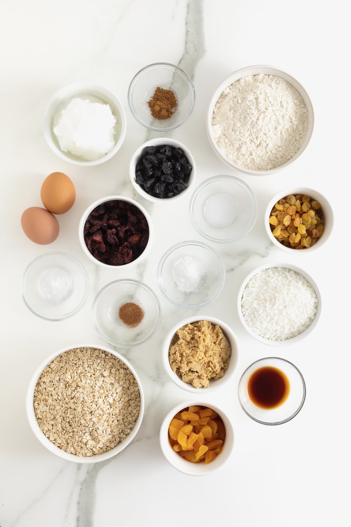 Ingredients to make coconut oatmeal cookies in small glass dishes on a white marble counter.