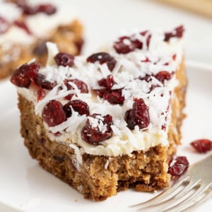 A cookie bar topped with white chocolate, coconut flakes and dried cranberries on a white rimmed plate.