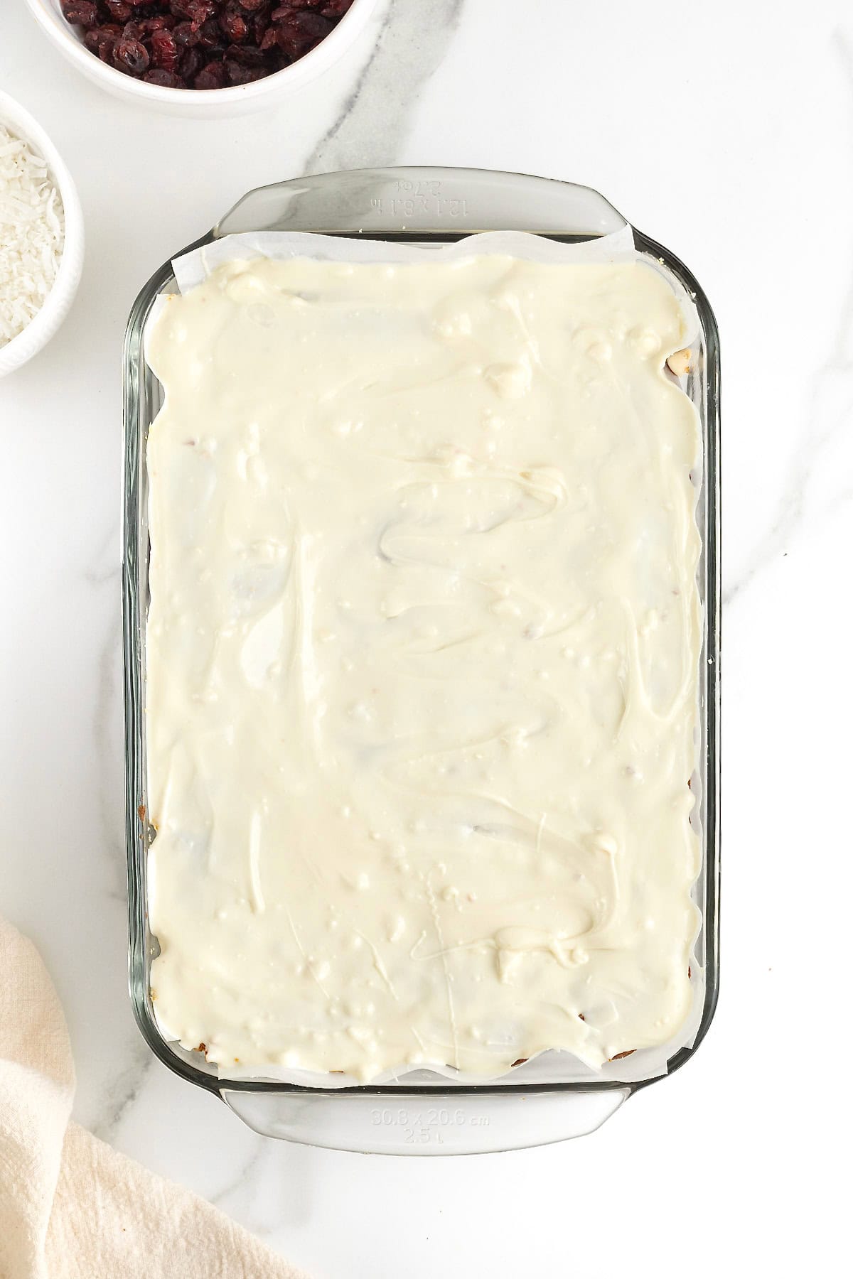 A parchment lined glass baking dish with baked cookie bars topped with melted white chocolate.