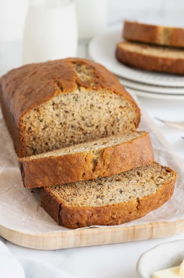 A loaf brown butter banana bread loaf on a parchment covered wooden cutting board.