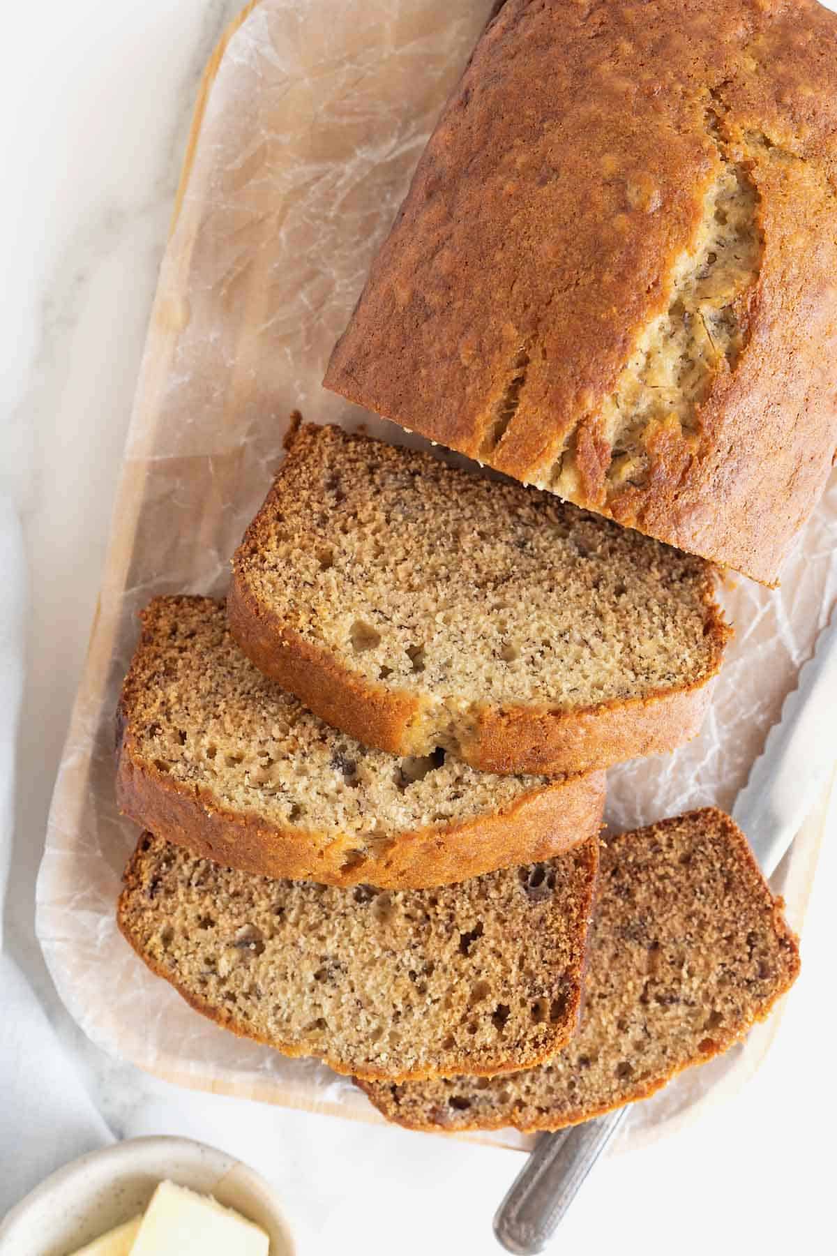 A sliced loaf brown butter banana bread loaf on a parchment covered wooden cutting board.
