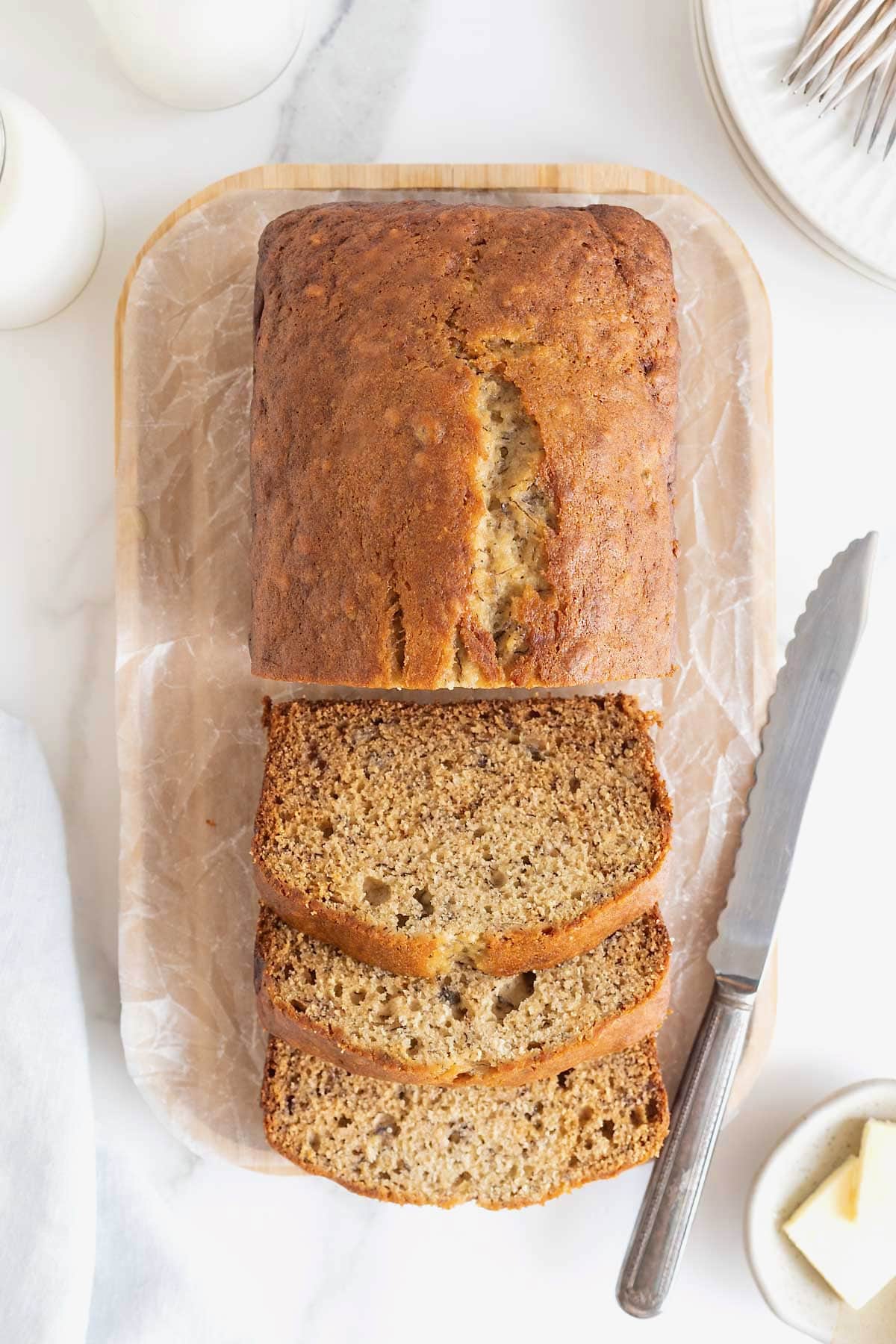 A sliced loaf brown butter banana bread loaf on a parchment covered wooden cutting board.