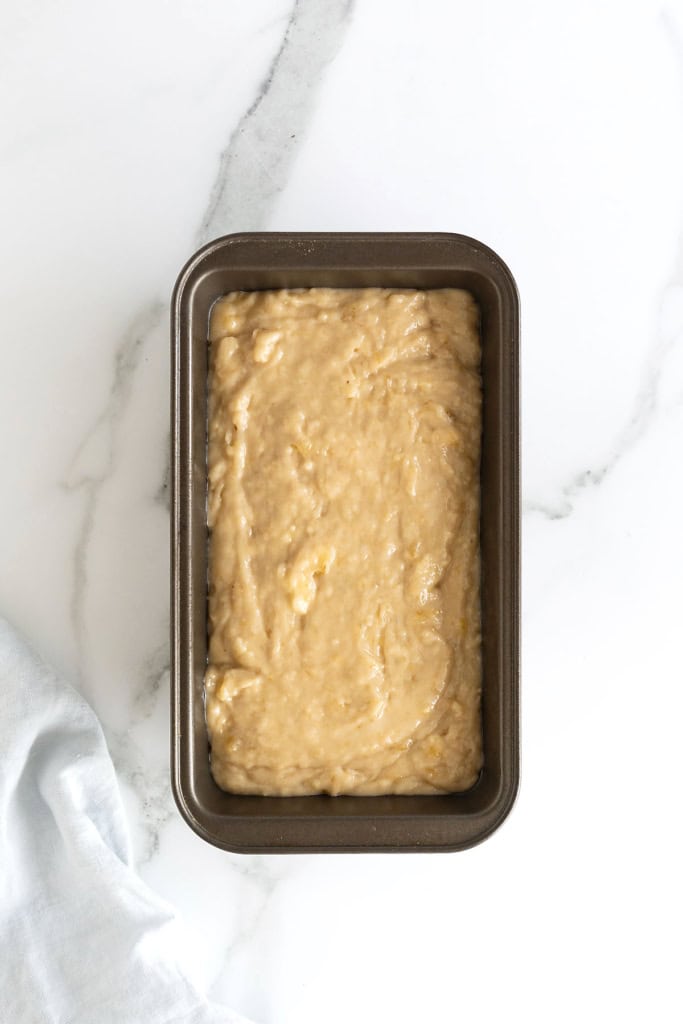 Banana bread batter in a dark aluminum loaf pan.