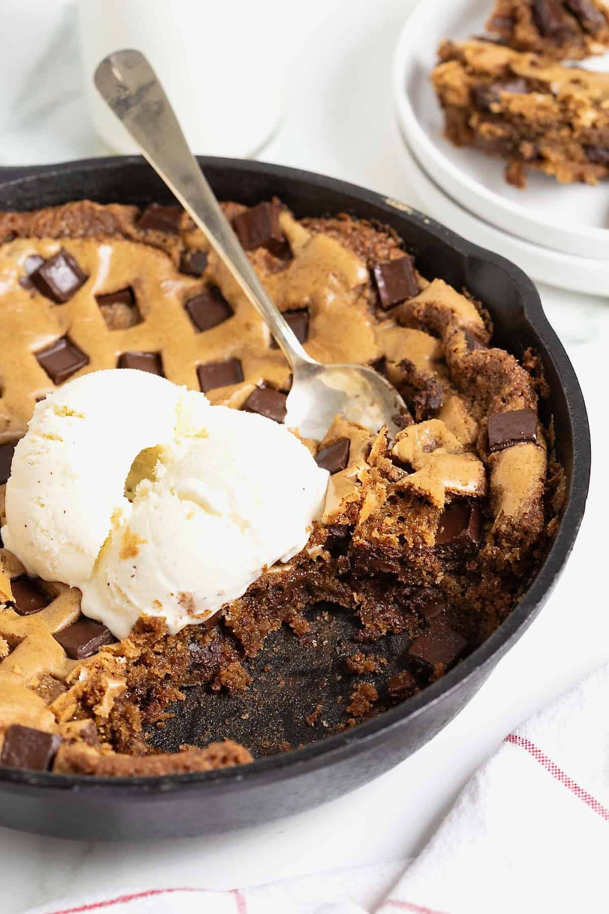 A chocolate chunk cookie in a large black skillet. There's a scoop of ice cream on top and a spoon stuck in it.