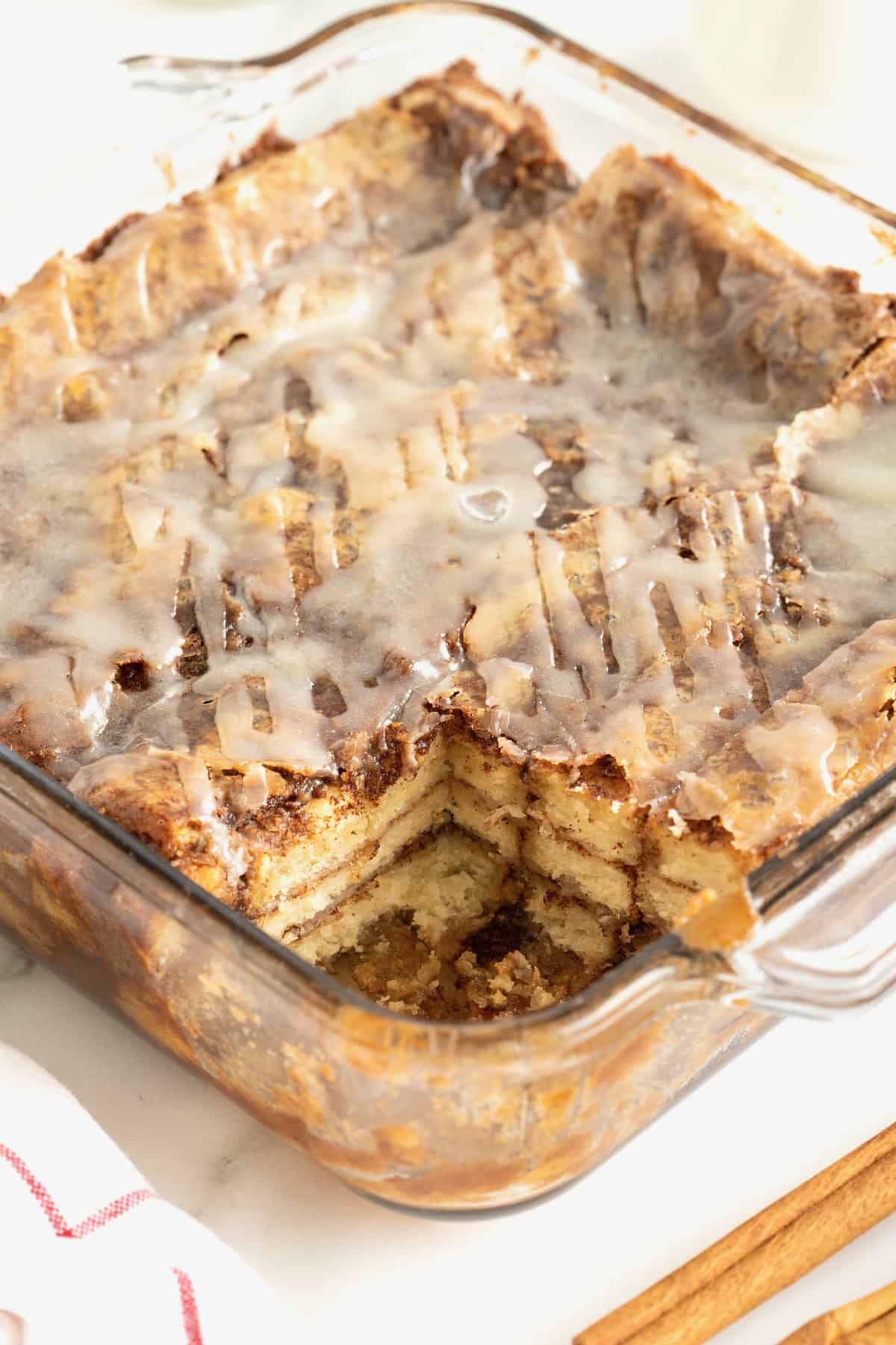A square glass baking dish of cinnamon roll lasagna. The bottom right square piece is missing.