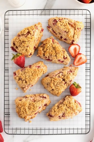 7 strawberry scones topped with streusel on a parchment lined cooling rack.