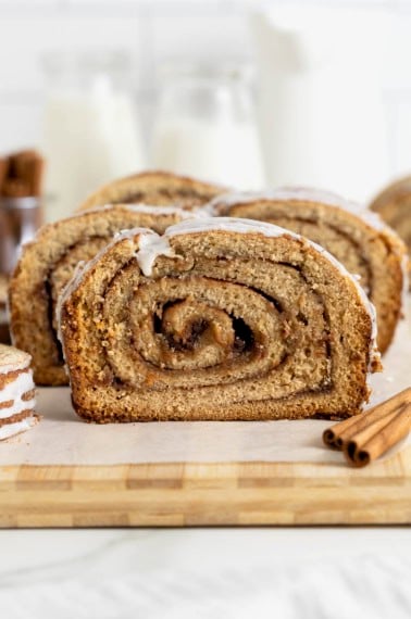 A loaf of cinnamon roll bread sliced on a parchment lined wooden cutting board.